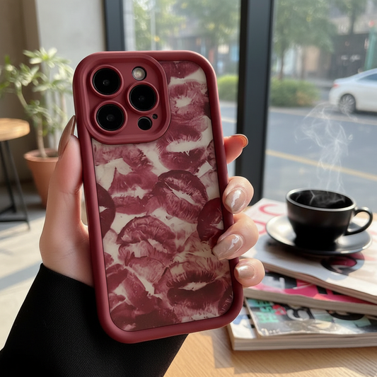 Phone case with lip print design held by a hand, with a coffee cup and magazine in the background.